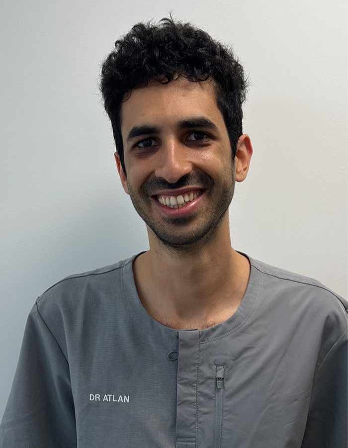 Uśmiechnięty dentysta Simon Atlan w szarym uniformie medycznym. 